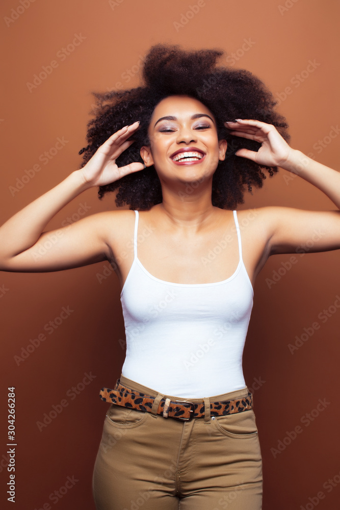 pretty young african american woman with curly hair posing cheerful gesturing on brown background, lifestyle people concept