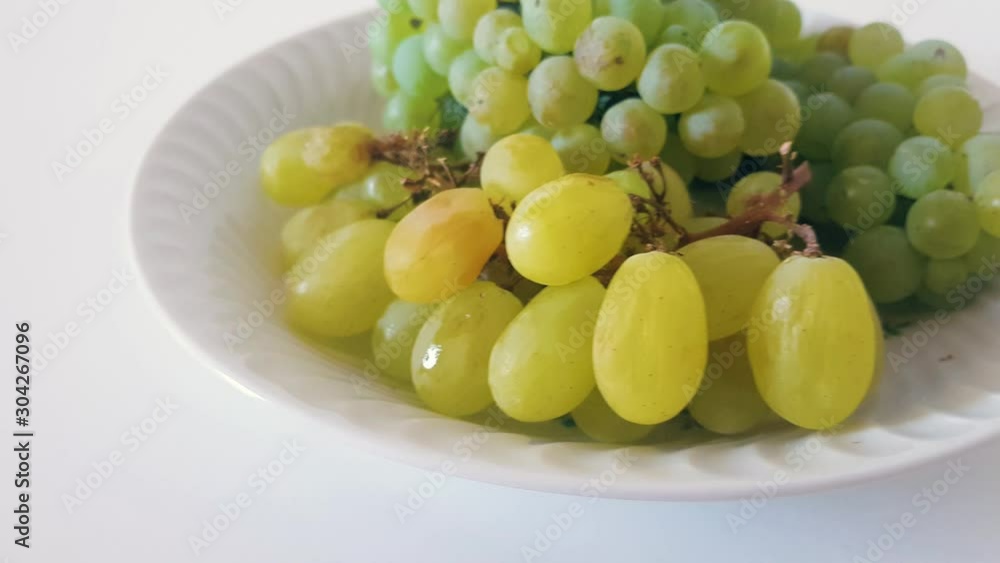 Bunch of green grapes in white plate isolated on white background.Panning left. Bunch of green grapes in white plate isolated on white background.Panning left.