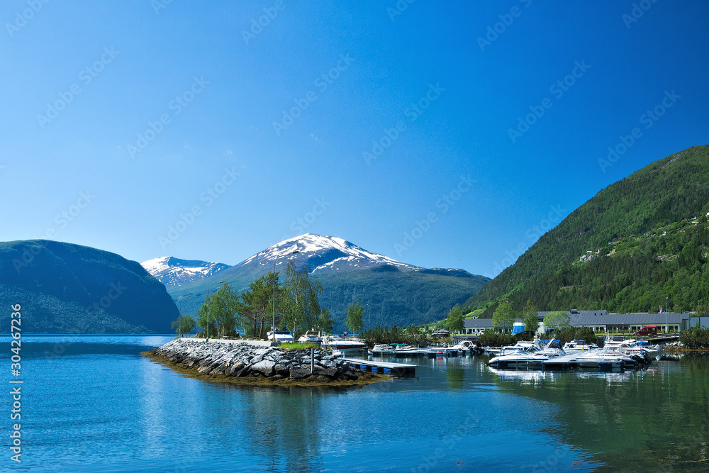 Beautiful boat marina in Valldal, Norway and fjord on a sunny day with snow on the peaks of spectacular nearby mountains. Breathtaking.