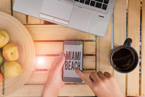 Handwriting text writing Miami Beach. Conceptual photo the coastal resort city in MiamiDade County of Florida woman computer smartphone drink mug office supplies technological devices photo