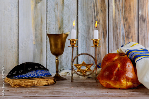Shabbat with challah bread on a wooden table candles and cup of wine.
