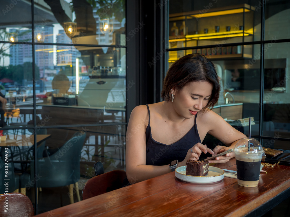 Beautiful Asian woman short hair using smartphone and drinking coffee and dessert at cafe. Beautiful Asian woman short hair using smartphone and drinking coffee and dessert at cafe.