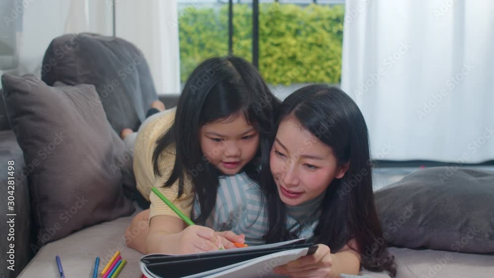 Asian middle-aged woman teach her daughter do homework and drawing at home. Lifestyle mother and kid happy fun spend time together in living room in modern home in the evening concept. Asian middle-aged woman teach her daughter do homework and drawing at home. Lifestyle mother and kid happy fun spend time together in living room in modern home in the evening concept.