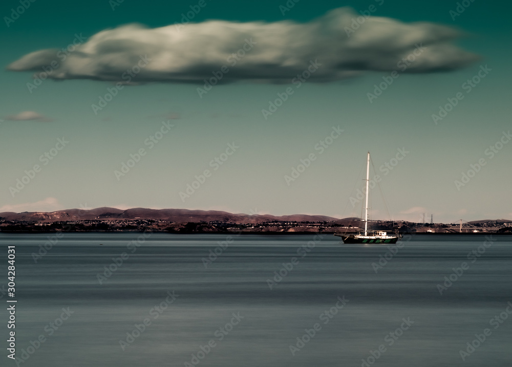 Solitary sailboat moored in quiet bay under a single cloud