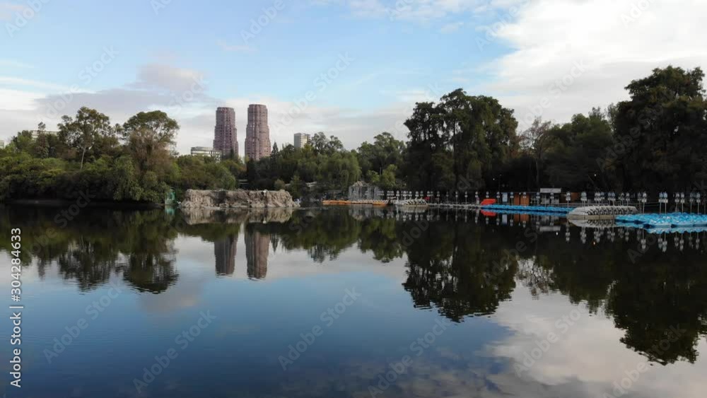The skyline of Polanco reflecting at Chapultepec Lake at sunrise. Drone flying forward with a blue skye as background