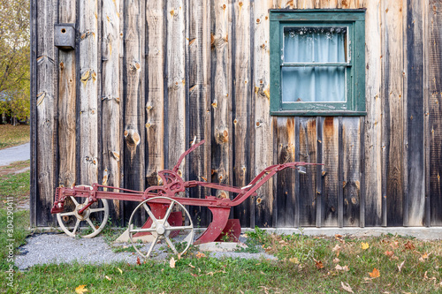 old unused farm equipment leaning against a weather beaten cabin wall photo
