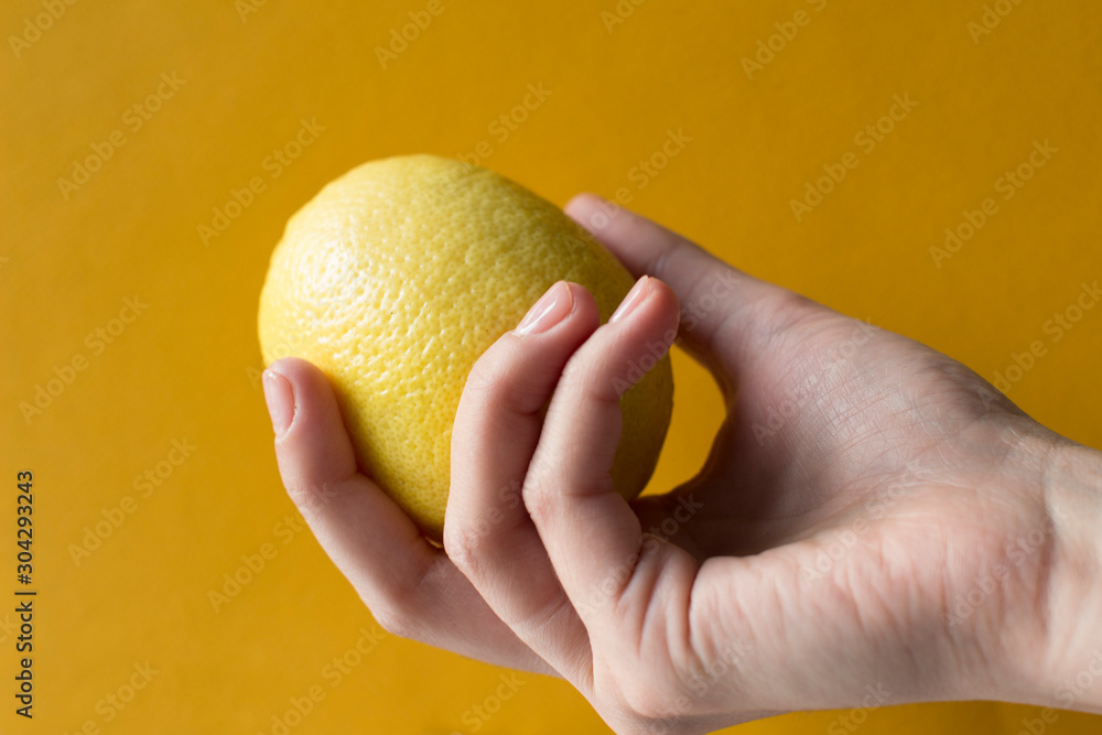 young woman holding a whole lemon on yellow background young woman holding a whole lemon on yellow background