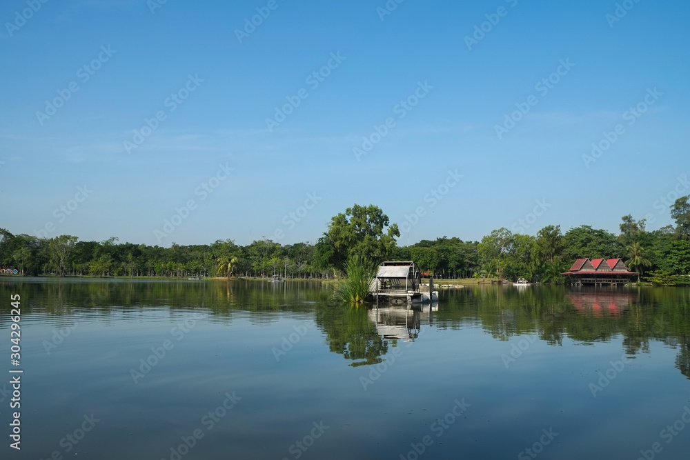 Scenic view of a park in the city with a pond, green tree and blue sky, calm and relax. Trees and sky reflecting in water Scenic view of a park in the city with a pond, green tree and blue sky, calm and relax. Trees and sky reflecting in water