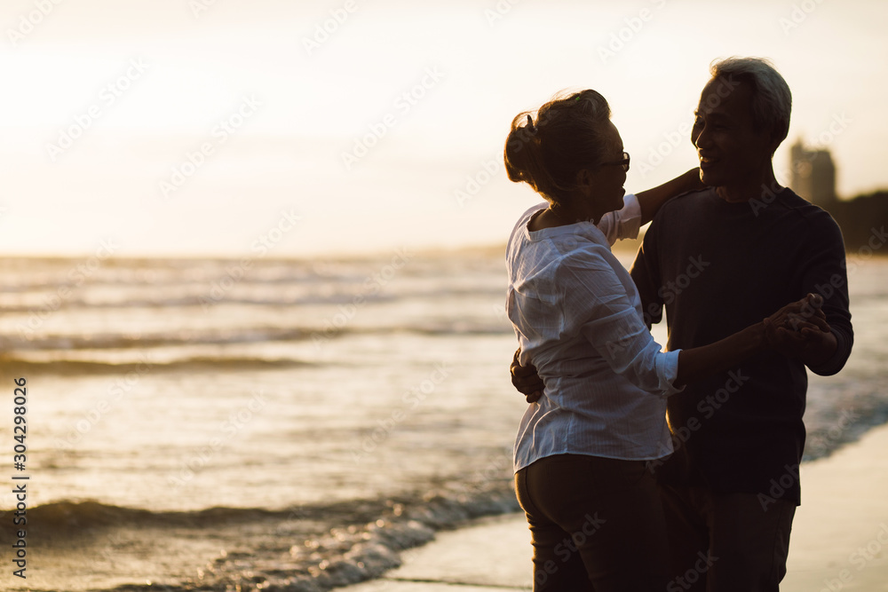 Romantic senior couple dancing together on beach at dusk sunset. Retirement age concept and love