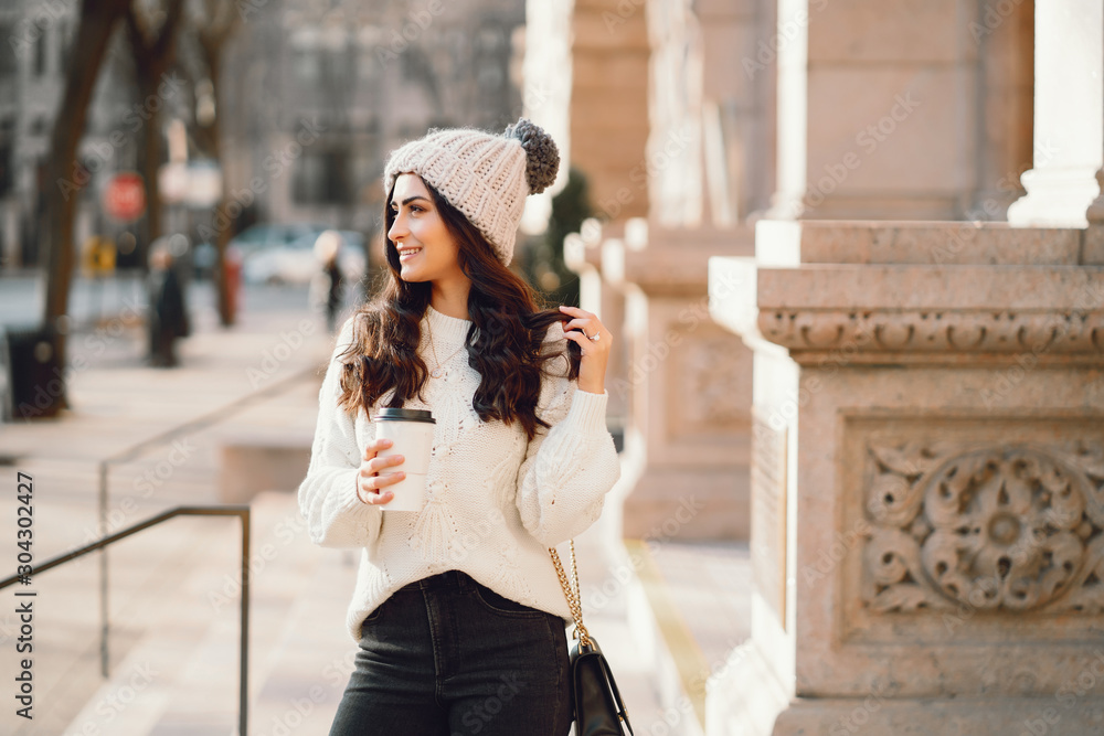 Elegant girl standing in a winter city. Woman in a white knited sweater. Beautiful lady with dark hair.