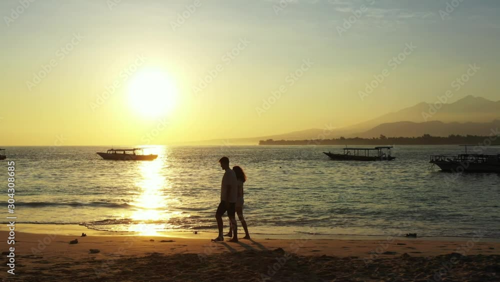 Playful young couple walking around exotic beach on a quiet evening with sun setting down sea horizon reflecting over lagoon full of boats in Jamaica Playful young couple walking around exotic beach on a quiet evening with sun setting down sea horizon reflecting over lagoon full of boats in Jamaica