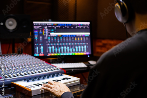 Φωτογραφία back of asian male music producer arranging a song on midi keyboard and computer in home recording studio