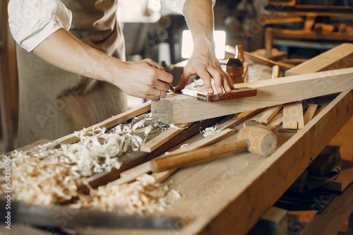Man working with a wood. Carpenter in a white shirt