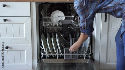 A woman opens a dishwasher and takes out clean dishes