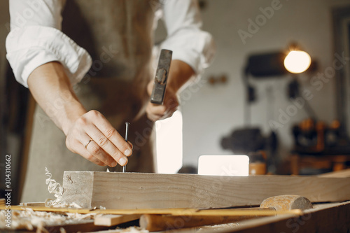 Man working with a wood. Carpenter in a white shirt. Man hammering nails into the wood