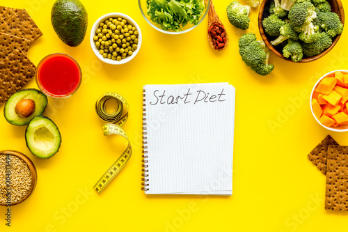 Diet program mockup. Start diet text in notebook near vegetables on yellow background top view