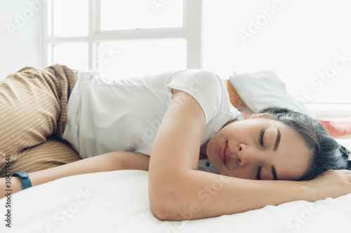 Asian woman is sleeping on her white cozy bed.