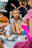 portrait of a little girl in a dress sitting on the floor surrounded by children listening attentively