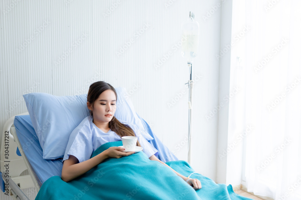 asian young female patient on bed with hand holding a cup coffee or tea in hospital background
