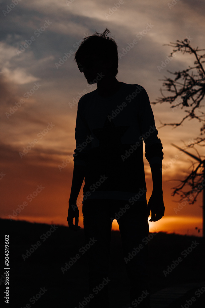 Silhouette of a man standing in front of trees and windmill during sunset