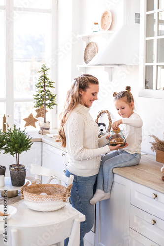 Mother and daughter eating Christmas biscuits at light kitchen.