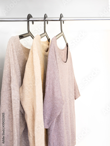 Knitted Sweaters and cardigans in beige grey neutral tone hanging in wardrobe. Fall winter season cloth concept.