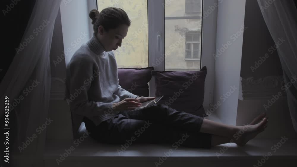 Girl sitting near the window uses a computer tablet. Monitor glows green. Green screen hromakey. For video editing replacement. Video footage Girl sitting near the window uses a computer tablet. Monitor glows green. Green screen hromakey. For video editing replacement. Video footage