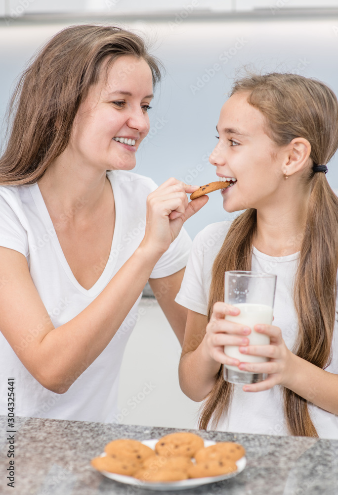 Happy family at home. Mother and daughter having breakfast with milk in the kitchen Happy family at home. Mother and daughter having breakfast with milk in the kitchen