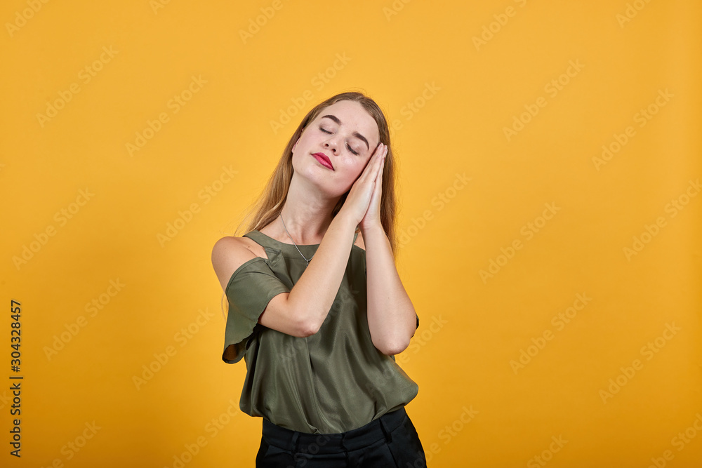 Gorgeous young caucasian girl making sleep gesture in dorable expression wearing pretty haki shirt on isolated yellow background Gorgeous young caucasian girl making sleep gesture in dorable expression wearing pretty haki shirt on isolated yellow background