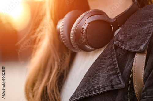 Stylish casual fashionable hipster student woman teenager with black wireless headphones while walking around the city. Lover music enjoys listening music © Goffkein