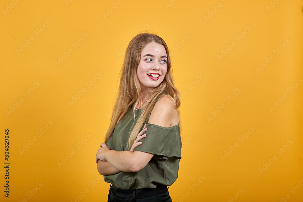 Smiling young woman in casual clothes holding hands crossed, loking aside, isolated on orange wall background. People sincere emotions, lifestyle concept. Smiling young woman in casual clothes holding hands crossed, loking aside, isolated on orange wall background. People sincere emotions, lifestyle concept.