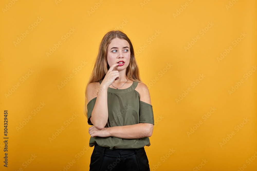 Young pretty attractive woman looking aside, opened eyes with the hand on mouth on isolated orange background wearing fashion clothes Young pretty attractive woman looking aside, opened eyes with the hand on mouth on isolated orange background wearing fashion clothes