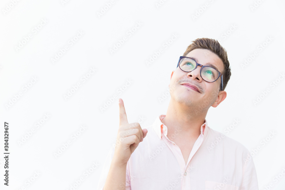 Positive pensive guy in eyewear looking and pointing finger up. Young man in glasses standing isolated over white background. Promotion concept Positive pensive guy in eyewear looking and pointing finger up. Young man in glasses standing isolated over white background. Promotion concept