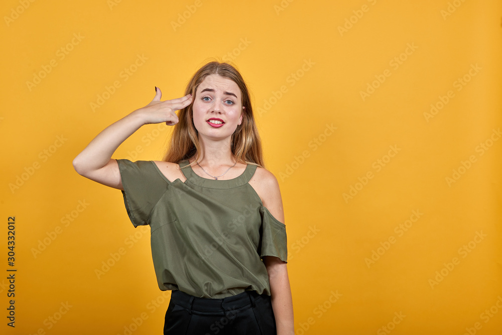 Young beautiful caucasian woman keeping hands on head, looking serious, model wearing fashion shirt on isolated orange background Young beautiful caucasian woman keeping hands on head, looking serious, model wearing fashion shirt on isolated orange background