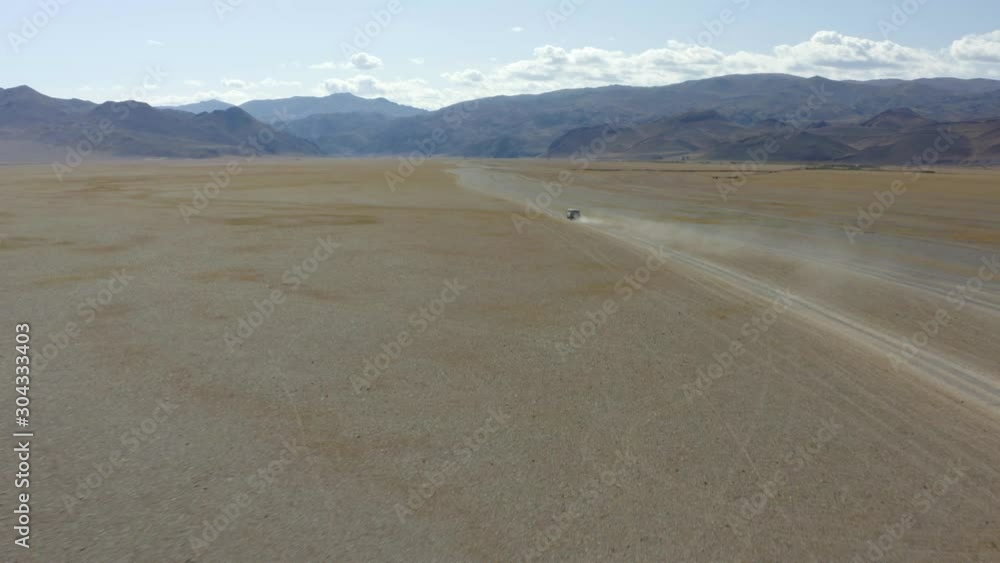 Aerial, tilt up, drone shot, of a van, on a road, in middle of a desert, in the Altai mountains, sunny day, near Bayan-Olgii, in Mongolia Aerial, tilt up, drone shot, of a van, on a road, in middle of a desert, in the Altai mountains, sunny day, near Bayan-Olgii, in Mongolia