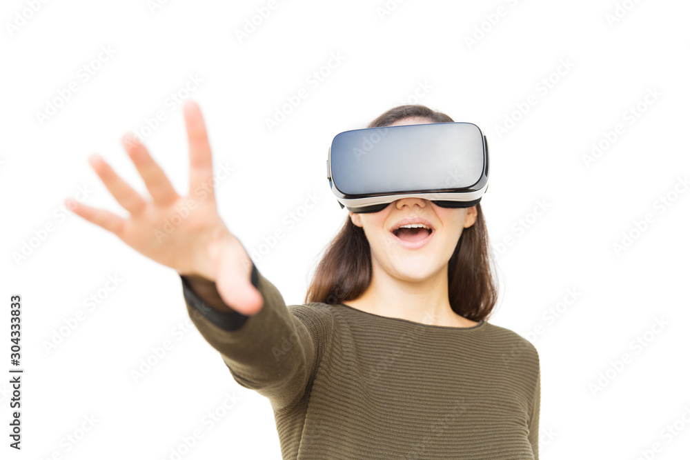 Happy excited student in VR headset touching air and shouting. Young woman in casual and virtual reality glasses standing isolated over white background. VR experience concept