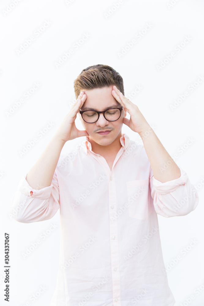 Tired stressed guy with closed eyes holding head. Young man in glasses standing isolated over white background. Suffering from headache concept Tired stressed guy with closed eyes holding head. Young man in glasses standing isolated over white background. Suffering from headache concept