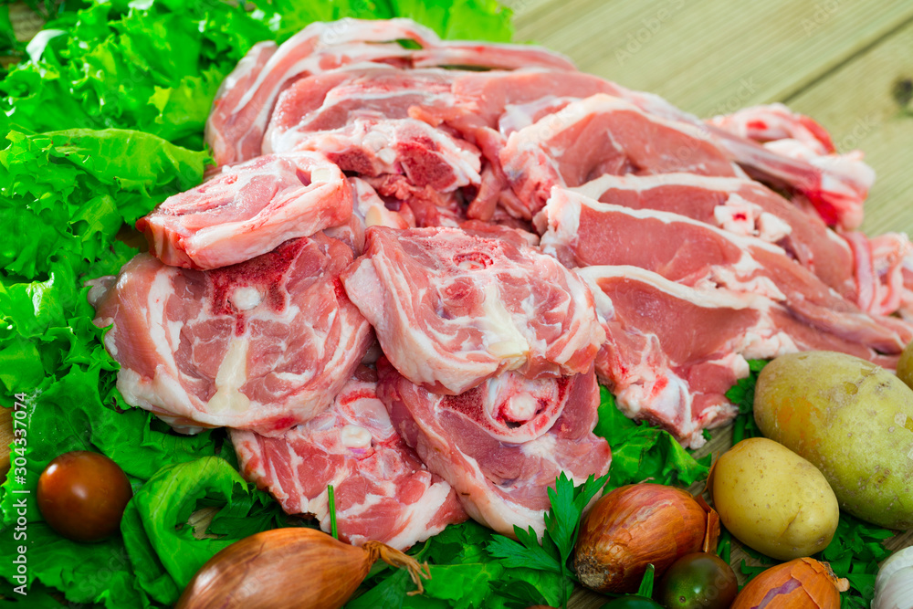 Pieces of fresh lamb meat on a wooden desk with  vegetables