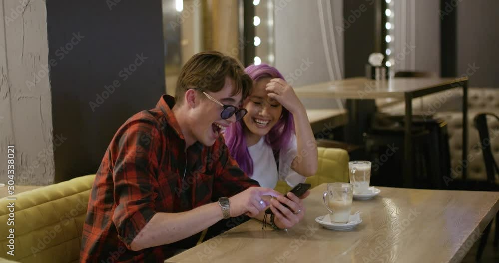 Young people communicate and use a smartphone in caffe, evening in the city, teens looking through photos on mobile phone. Young people communicate and use a smartphone in caffe, evening in the city, teens looking through photos on mobile phone.
