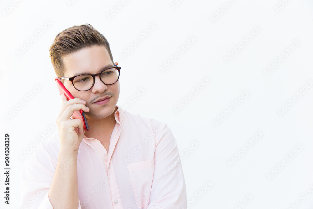 Serious guy in eyeglasses discussing problems on cell and looking away. Young man in glasses standing isolated over white background. Communication concept