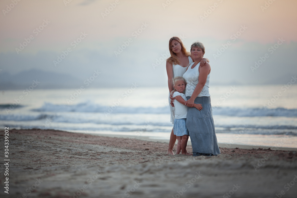 Portrait of happy mother and daughters. They hug on the background of the sea.