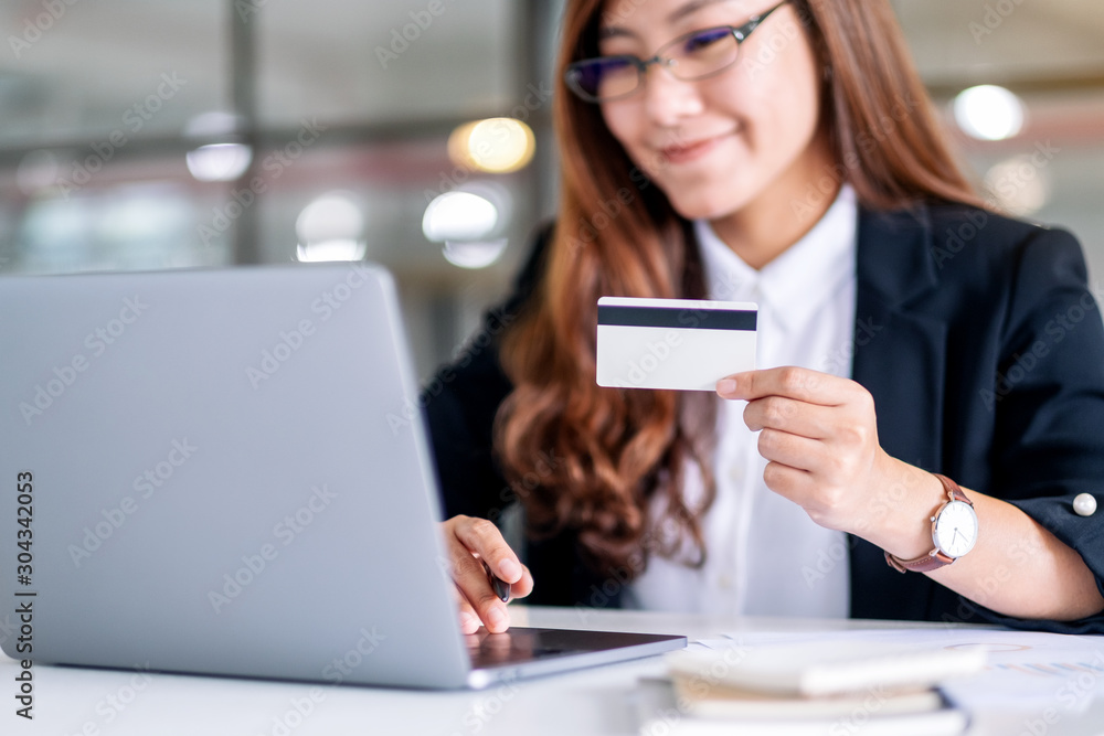 An asian businesswoman holding credit cards while using laptop computer in office An asian businesswoman holding credit cards while using laptop computer in office