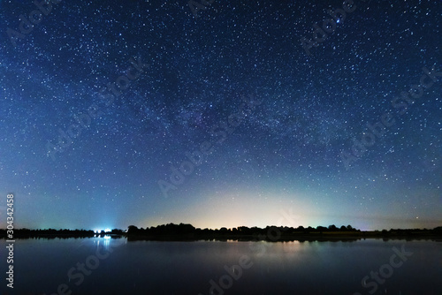 A magical starry night on the river bank with a large tree and a milky way in the sky and falling stars in the summer. © reme80