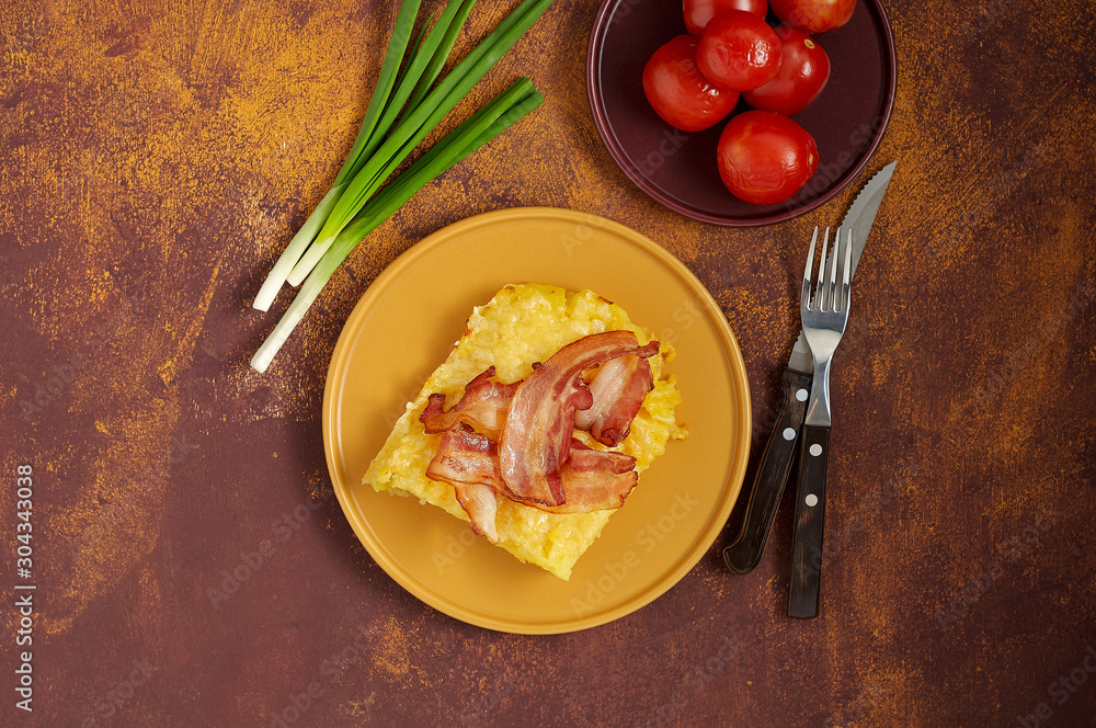 Cheesy potato bake with fried bacon, pickled tomatoes and green onion on yellow plate