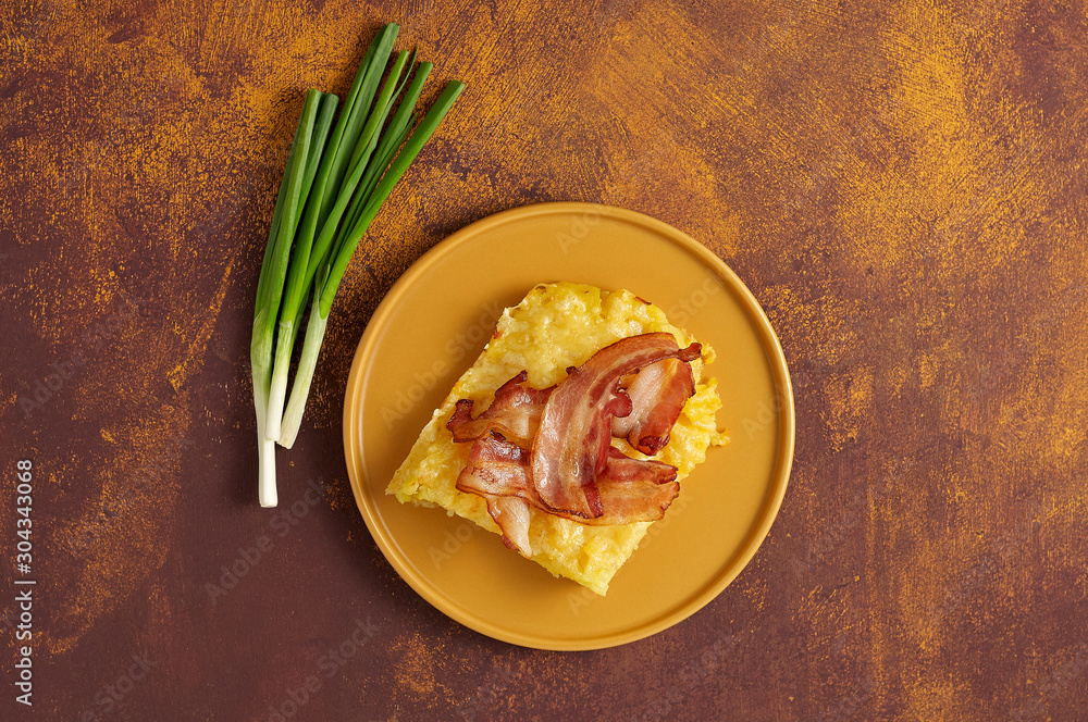 Cheesy potato bake with fried bacon and green onion on yellow plate