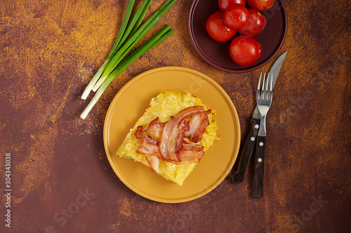 Obraz na płótnie Cheesy potato bake with fried bacon, pickled tomatoes and green onion on yellow plate w salonie