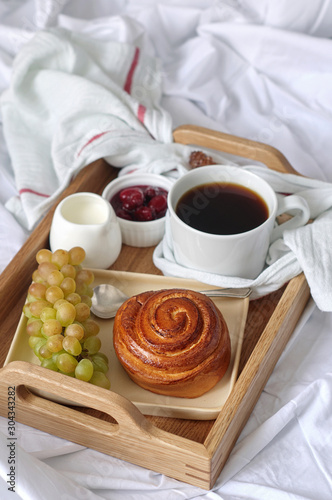 Obraz na płótnie Breakfast on white bed sheets in hotel room. Close up of wooden tray with coffee, bun, jam and grape w salonie