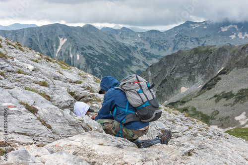Man helps to injured, wounded young boy, who lying among rocks in a mountain. Majestic peaks at background. Selective focus. First aid, survival concept, help someone in need.