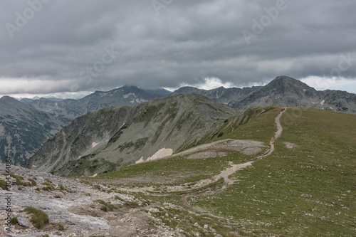 Tourists hiking at mountain on cloudy, stormy weather, on their way to Vihren peak, national park Pirin. Majestic bulgarian mountains. Selective focus. Healthy lifestyle concept, be active, adventure.