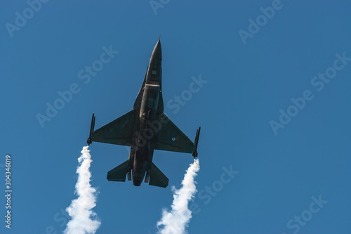 Canvas Print F-16 fighting military fighter jet airplane flying with smoke against blue sky background